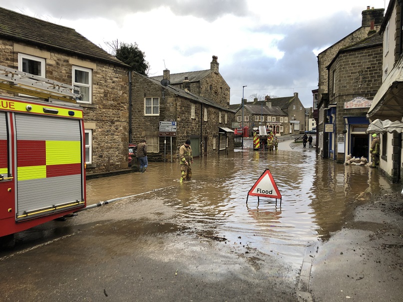 Photo of a flooded street with fire engines pumping water away